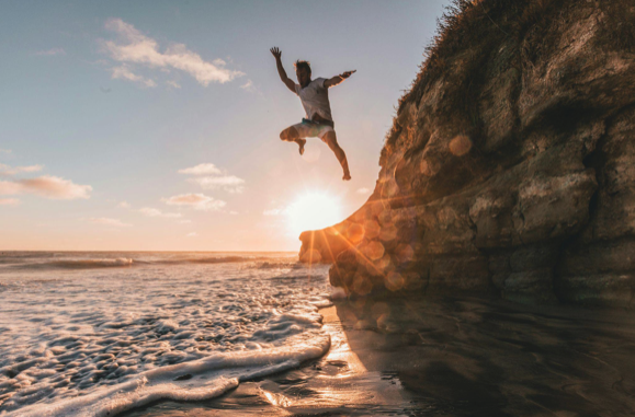 A person jumping off a short cliff into the ocean.